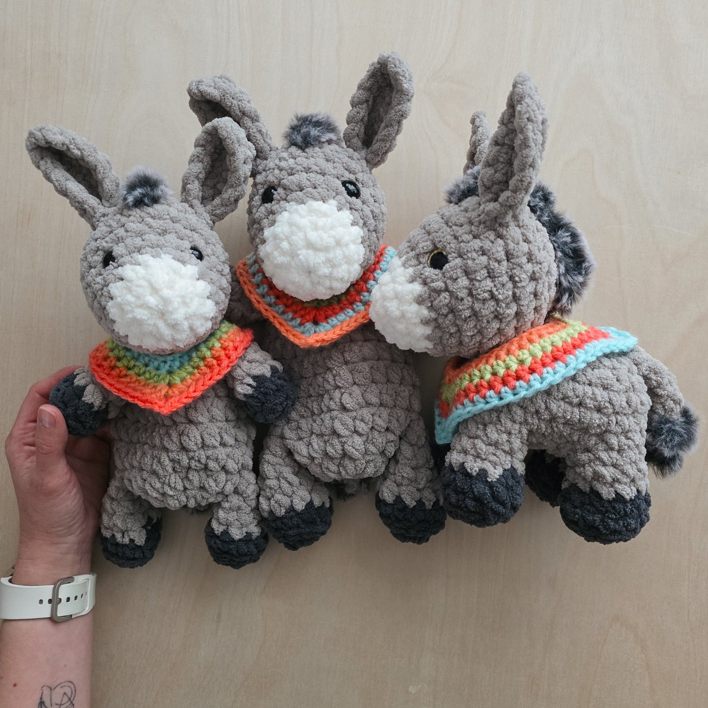 Three crocheted donkey toys with colorful scarves on a wooden surface.