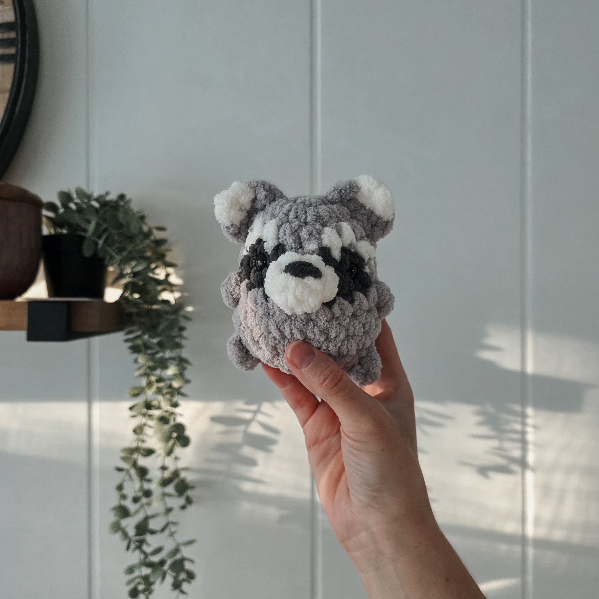 Hand holding a small gray plush toy against a white paneled wall.