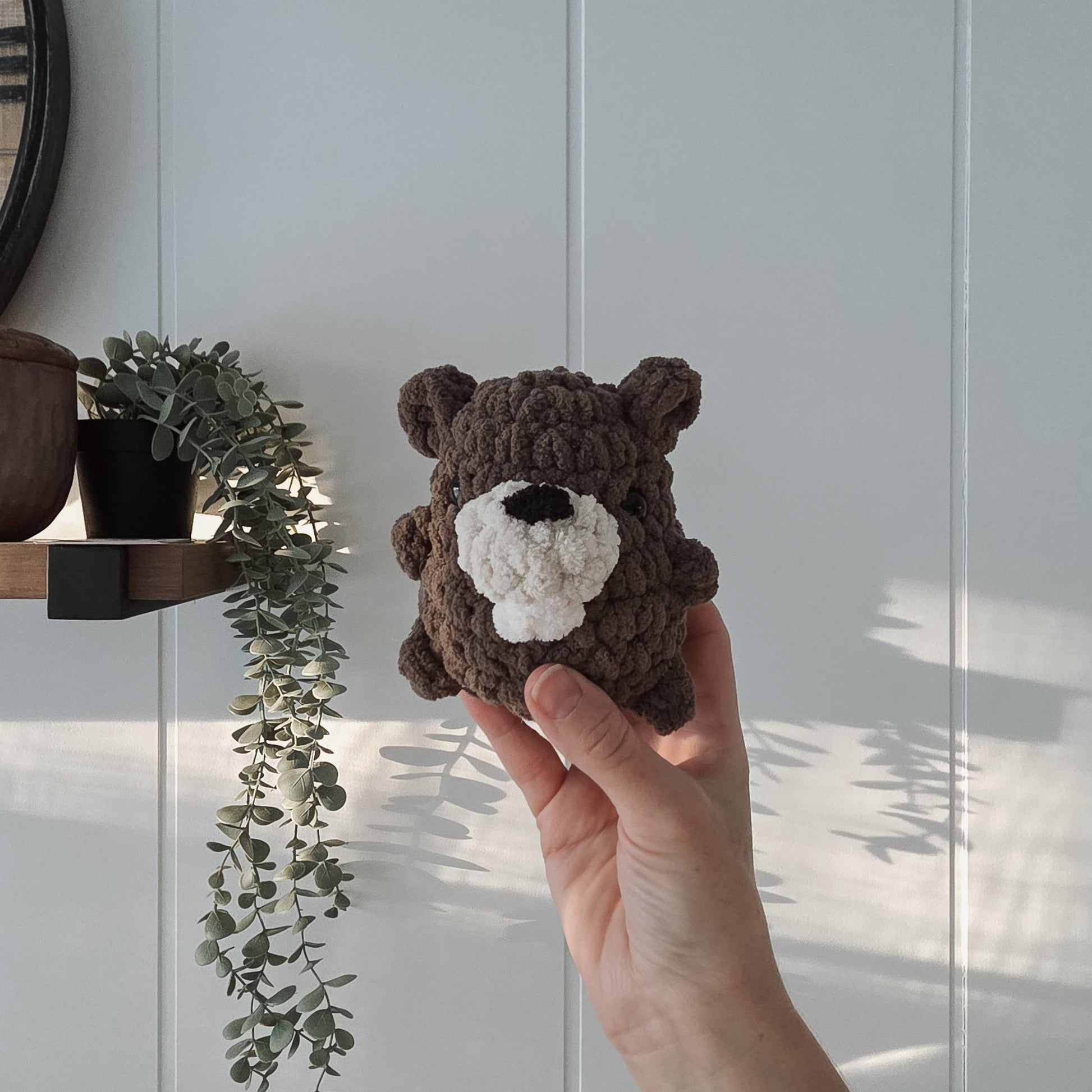 Hand holding a small brown beaver  crocheted toy against a light background