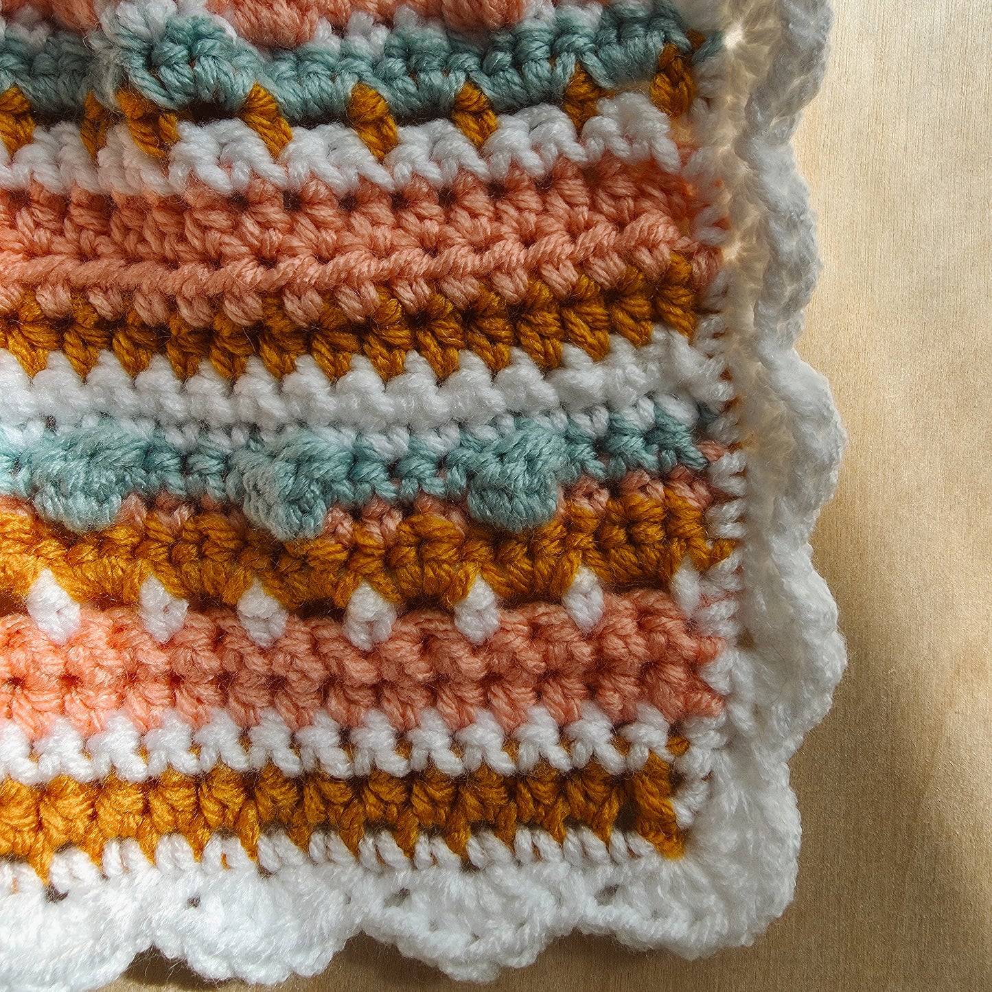 Close-up of a crocheted blanket with multicolored stripes on a wooden surface.