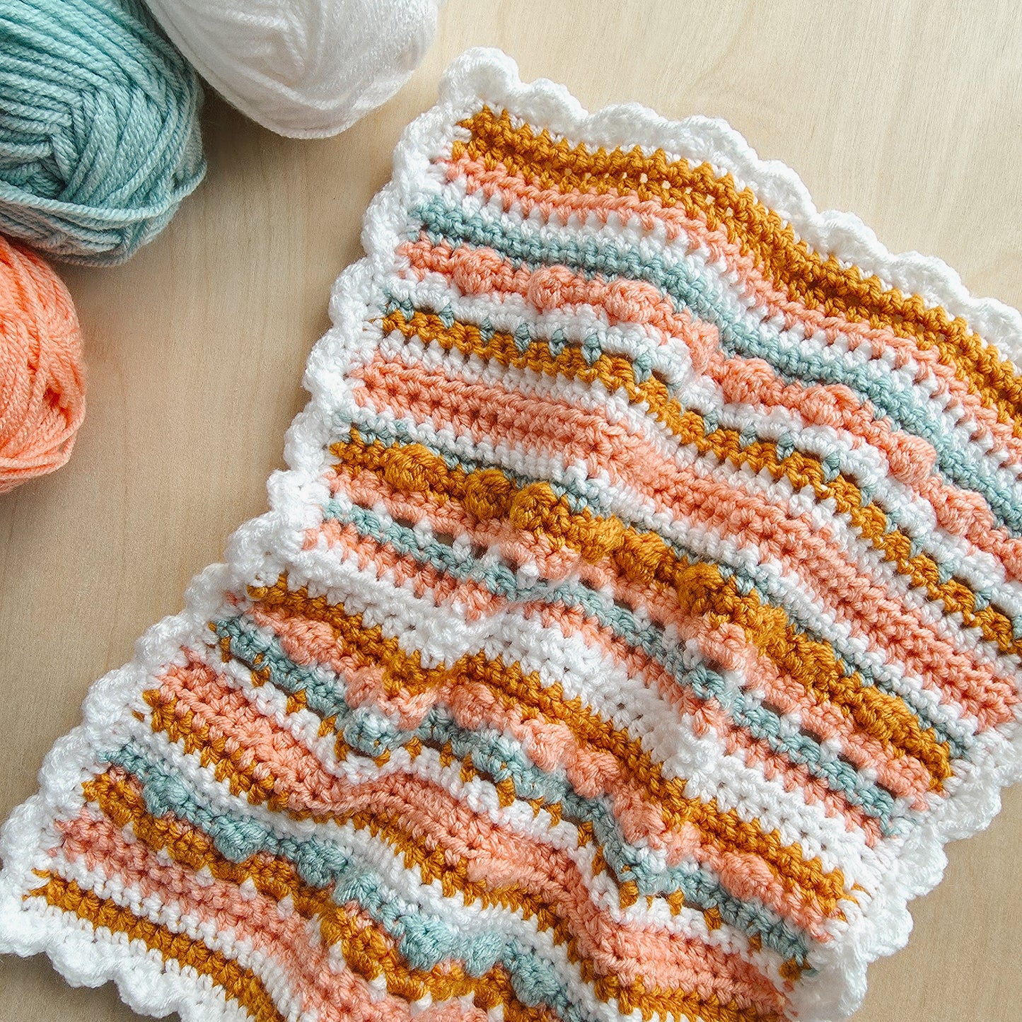 Knitted dishcloth with wavy pattern on a wooden surface with yarn balls.