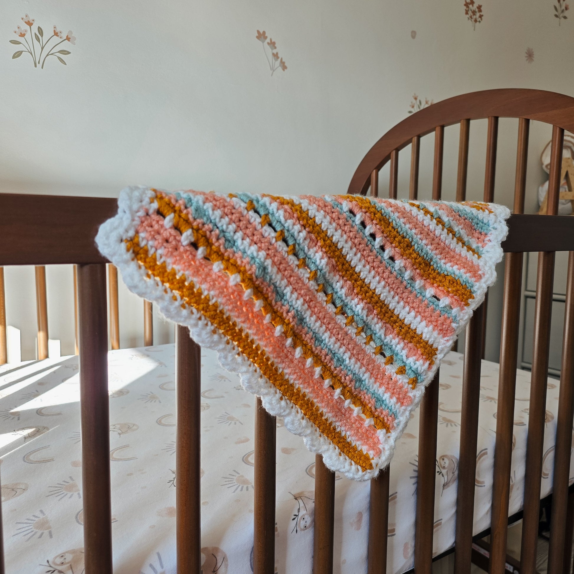 Striped baby blanket draped over a crib with floral wallpaper in the background