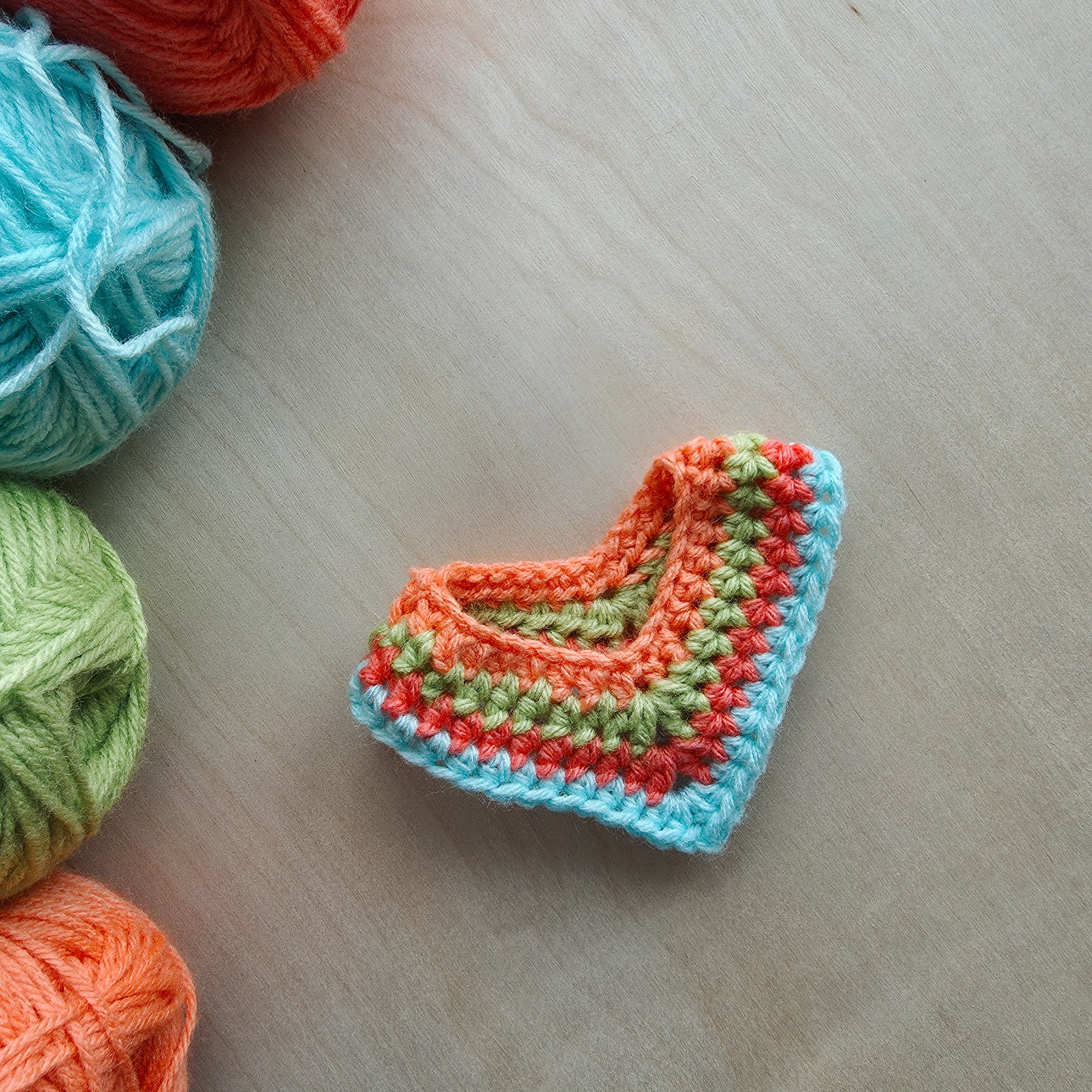 Crocheted poncho with colorful yarn on a wooden surface