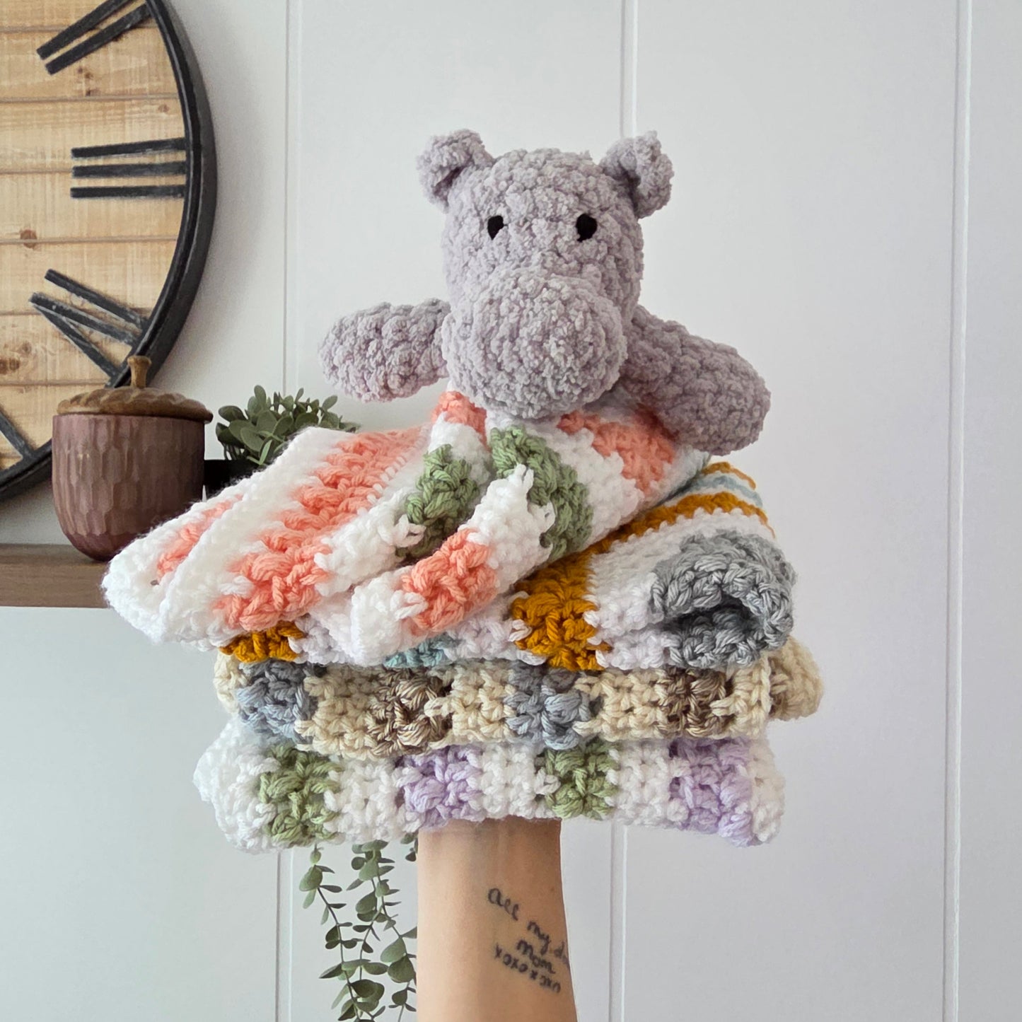 Collection of colorful crocheted scrunchies on a white surface with a wooden clock in the background.